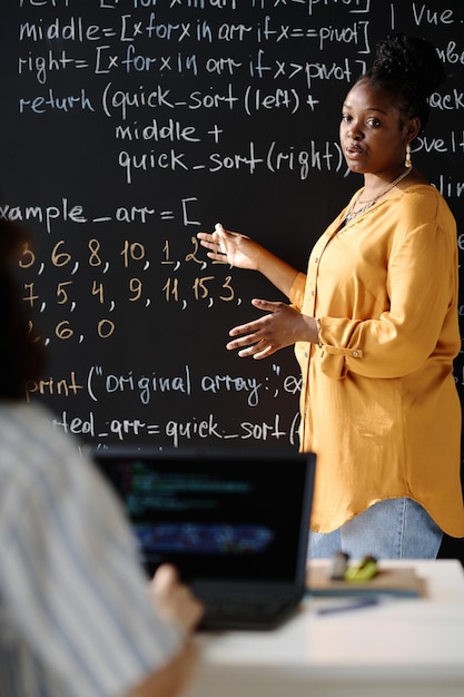 Immagine verticale del tutor afroamericano che punta alla lavagna e insegna l'IT allo studente durante la lezione