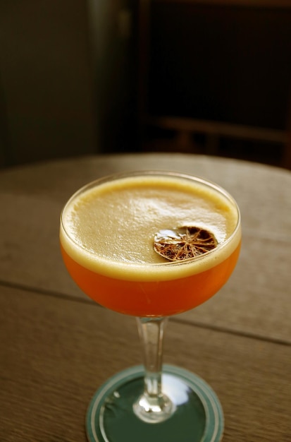 Immagine verticale di un bicchiere di cocktail arancione sulla tavola rotonda di legno