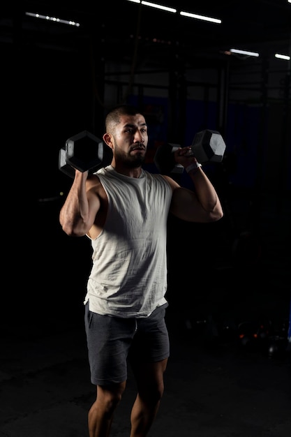 Immagine verticale di un uomo muscoloso che preme con un paio di manubri in palestra