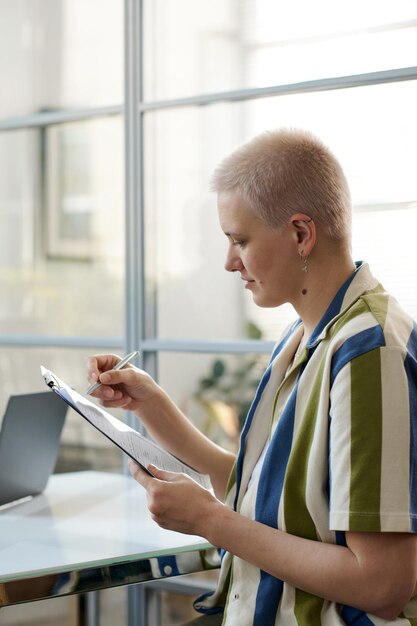 Immagine verticale di una giovane donna con la firma del contratto a testa rasata seduta in ufficio