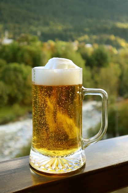 Immagine verticale di una pinta di birra alla spina sulla ringhiera del balcone con vista sfocata della foresta