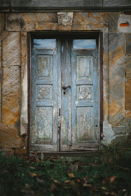 Immagine verticale di una vecchia porta di legno di un vecchio edificio circondato dal verde e dalla sporcizia