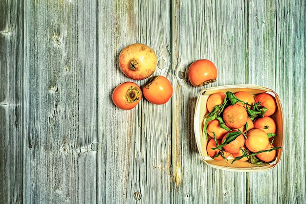 Immagine vista dall'alto del cesto di legno con mandarini di frutta matura con cachi foglie verdi e melograno su assi di legno