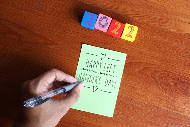 Immagine vista dall'alto della mano sinistra scrivi testo Happy Left Handers Day su carta verde su tavolo di legno