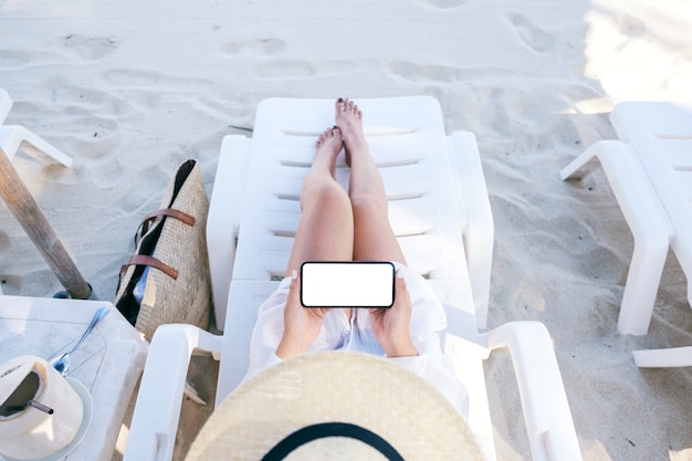 Immagine vista dall'alto di una donna che tiene e usa un telefono cellulare bianco con uno schermo desktop vuoto mentre è sdraiata su una sedia a sdraio