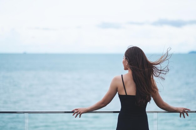 Immagine vista posteriore di una bellissima giovane donna asiatica in piedi e guardando il mare e il cielo blu