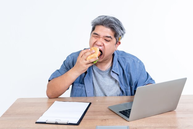 Immagini ritratto di uomini asiatici di mezza età d'affari stanno mangiando hamburger mentre stava lavorando utilizzando un computer portatile per il lavoro aziendale, per le persone e il concetto di cibo.