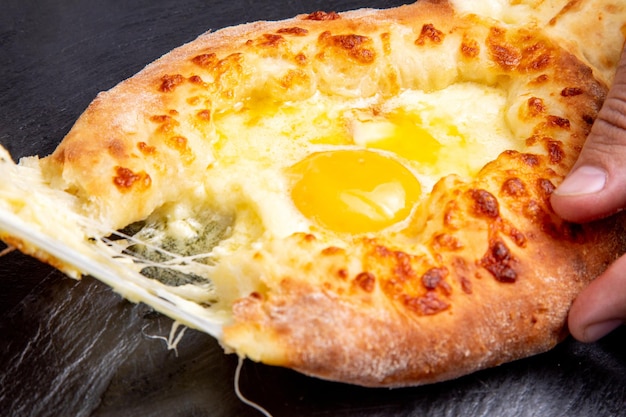 Immerge una fetta di khachapuri in un uovo su uno sfondo scuro