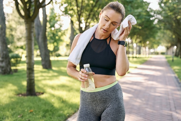 Impegnati ad essere in forma donna sportiva stanca in abbigliamento sportivo asciugandosi il sudore con un asciugamano e rinfrescando dopo