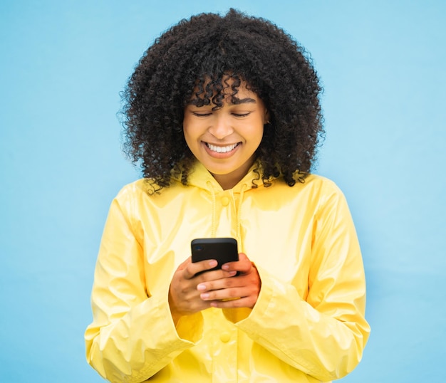 Impermeabile donna nera e telefono con una persona in inverno con sfondo blu studio Felicità isolata e comunicazione sui social media di una donna pronta per inviare messaggi e connettersi su un'app meteo