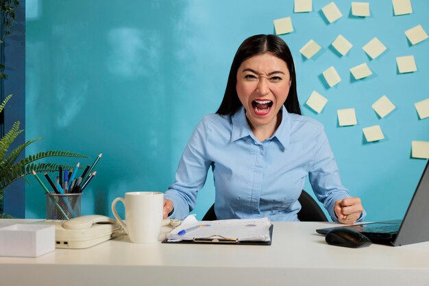 Impiegata aziendale femminile oberata di lavoro che esprime disperazione e stress gridando ad alta voce alla telecamera. Donna professionale con sentimenti negativi a causa del carico di lavoro esagerato.