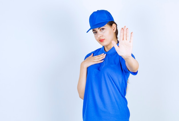 Impiegata della donna delle consegne in uniforme blu in piedi e che mostra il segnale di stop.