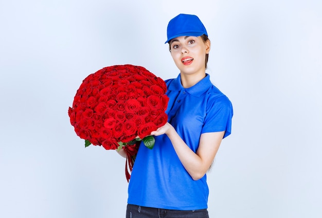 Impiegata della donna delle consegne in uniforme blu in piedi e con in mano un mazzo di rose.