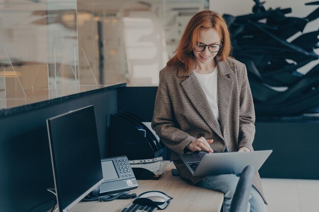 Impiegata femminile seduta sulla scrivania mentre lavora con i file di progetto in un laptop moderno