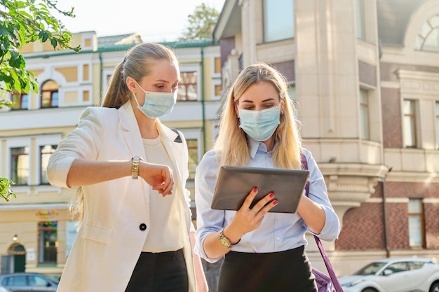 Impiegate due giovani donne d'affari che camminano lungo la strada della città indossando maschere protettive mediche. Stile di vita, affari in un'epidemia, pandemia, cattiva ecologia