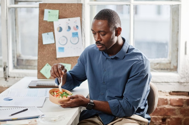 Impiegato afroamericano che mangia insalata per pranzo