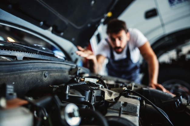 Impiegato barbuto dedito laborioso in tuta che fissa il motore. Non ha idea di cosa sia sbagliato.