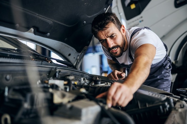 Impiegato barbuto dedito laborioso in tuta che ripara auto