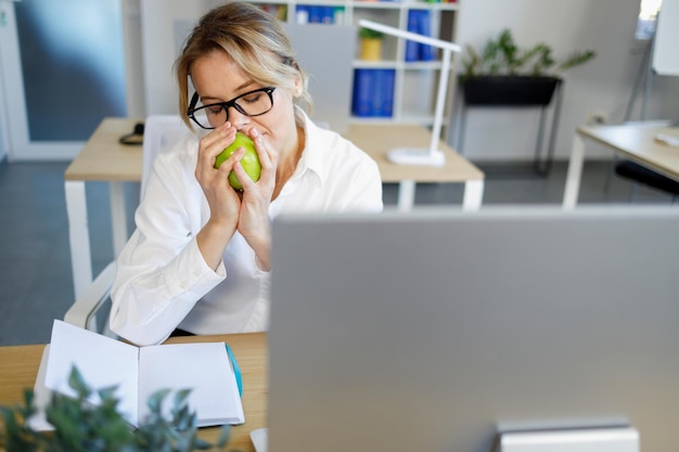 Impiegato che annusa una mela verde profumata mentre fa uno spuntino al lavoro