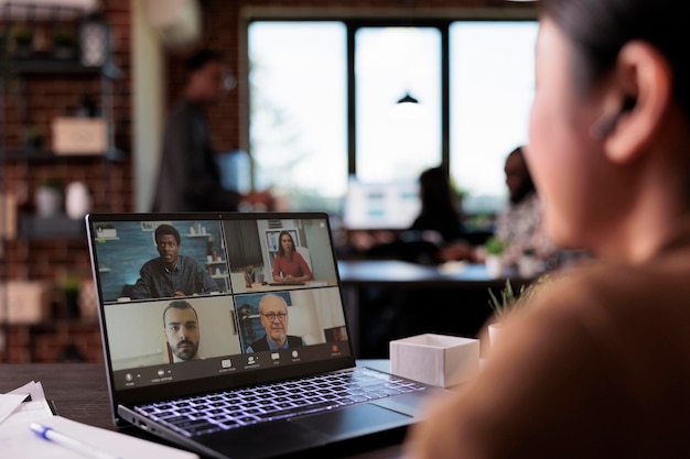 Impiegato dell'ufficio che utilizza il telelavoro per videochiamate per chattare con i colleghi sul laptop, parlando durante una riunione di videoconferenza remota. Conversazione Internet in webcam in teleconferenza online con le cuffie.