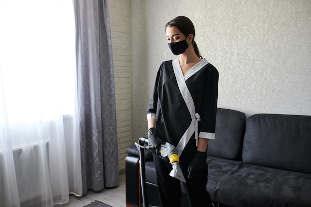 Impiegato della società di servizi di pulizia che rimuove lo sporco dai mobili in appartamento con attrezzatura professionale Divano per la pulizia del braccio della governante femminile con aspirapolvere