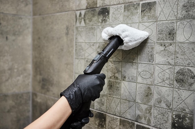 Impiegato della società di servizi di pulizia in guanti di gomma che puliscono le piastrelle in bagno con attrezzature professionali per la pulizia a vapore