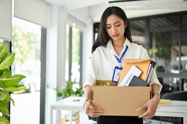 Impiegato femminile asiatico triste e frustrato che trasporta la sua appartenenza lasciando un lavoro