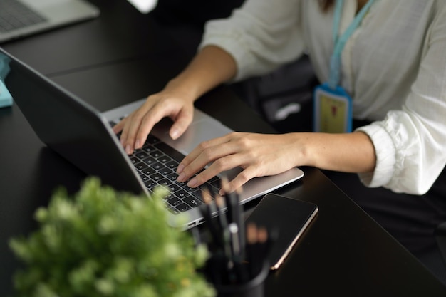 Impiegato femminile del primo piano che digita le sue informazioni di progetto sul computer portatile, lavorando nell'ufficio.