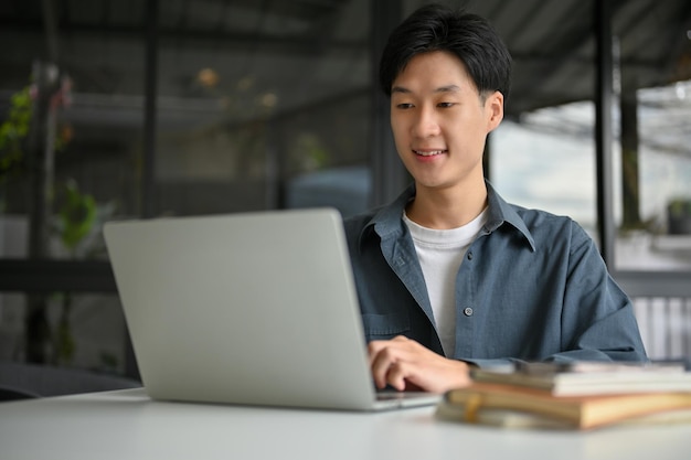 Impiegato maschio asiatico intelligente che lavora a distanza presso la caffetteria utilizzando il computer portatile