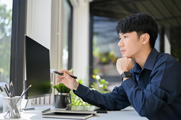 Impiegato o uomo d'affari maschio asiatico intelligente che si concentra sul suo compito guardando lo schermo del computer