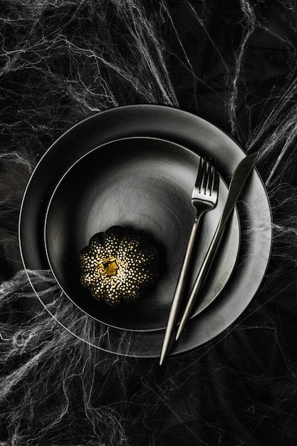 Impostazione della tabella di Halloween su sfondo scuro. Piatto su un tavolo nero con ragnatela. Concetto di vacanza alla moda piatto, vista dall'alto.