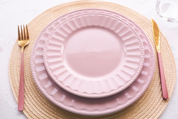 Impostazione della tabella. due piatti rosa vuoti, cucchiaio e forchetta su un tavolo bianco