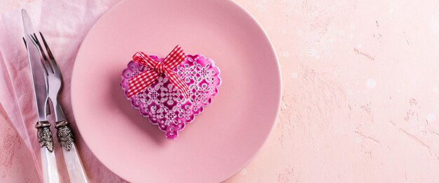Impostazione della tavola di San Valentino con piatto rosa e cuore regalo su sfondo rosa chiaro