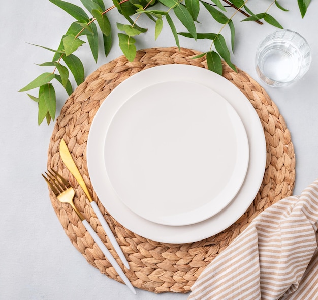Impostazione festiva della tavola con piatti bianchi vetro e posate su uno sfondo chiaro con tovaglioli e rami di eucalipto concetto del menu del ristorante Vista superiore