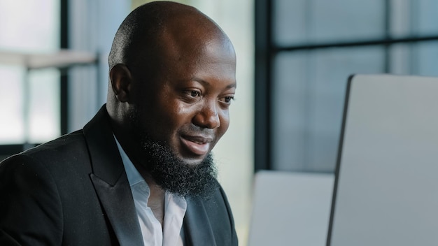 Imprenditore africano concentrato che digita sulla tastiera lavorando a distanza in ufficio guarda il monitor che studia