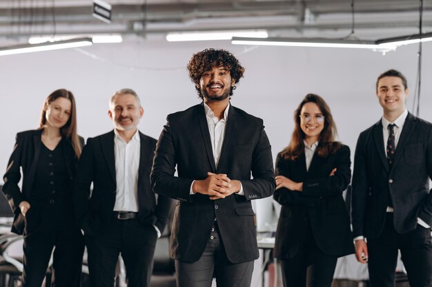Imprenditore ambizioso in piedi davanti ai suoi dipendenti Gruppo di imprenditori in posa con il sorriso Vista frontale del team di business multietnico