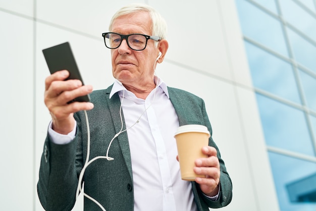 Imprenditore anziano con drink utilizzando smartphone