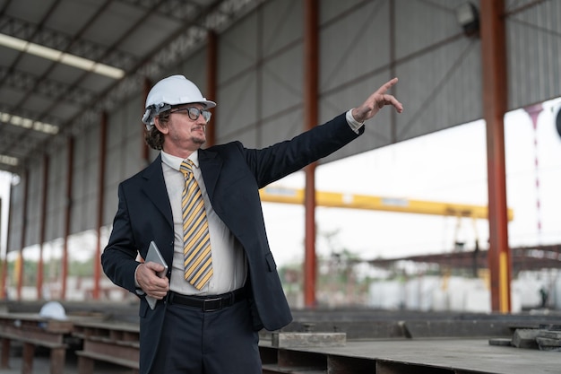 Imprenditore anziano indossa casco di sicurezza che tiene il tablet e indica la posizione nel cantiere