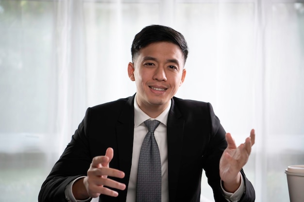 Imprenditore asiatico che usa i gesti delle mani per presentare un progetto parlando con cliente e collega