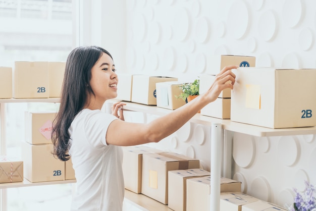 Imprenditore asiatico delle donne che lavora a casa con il contenitore di imballaggio sul posto di lavoro