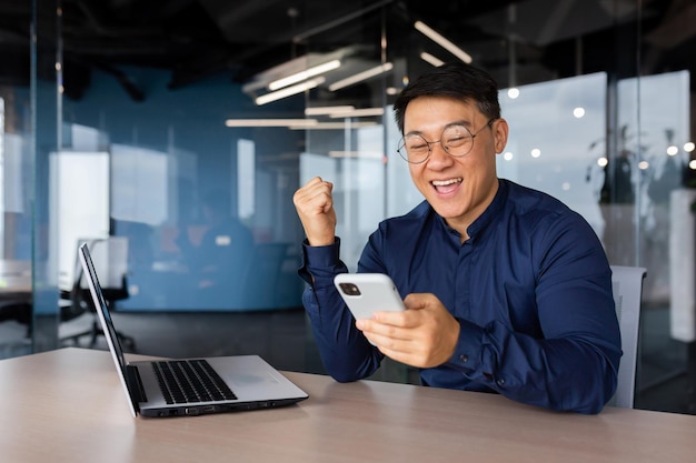 Imprenditore asiatico di successo che celebra la vittoria e la notifica di buone notizie dalla lettura del telefono