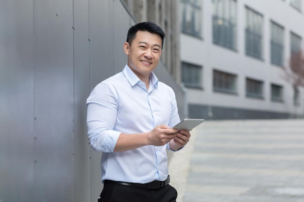 Imprenditore asiatico di successo con computer tablet in mano sorridente e guardando l'uomo della fotocamera