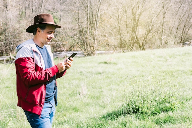 Imprenditore autonomo uomo che indossa un cappello guardando il suo telefono cellulare mentre ci si rilassa nel campo su un prato Concetto di lavoro godere relax Tecnologia Internet e connettività