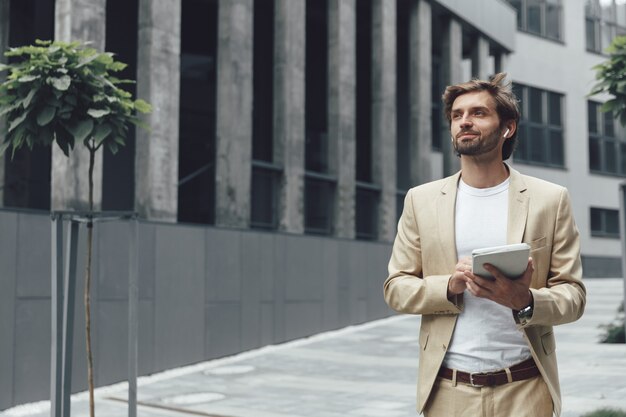 Imprenditore barbuto di successo vestito in abito alla moda lavorando su tavoletta digitale mentre si trovava all'aria aperta