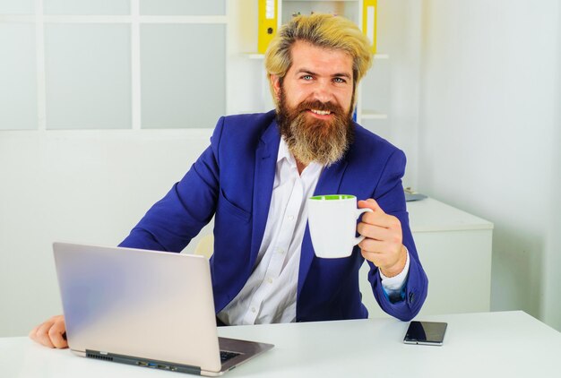 Imprenditore che lavora con il computer portatile in ufficio con una pausa caffè imprenditore con una tazza di cappuccino