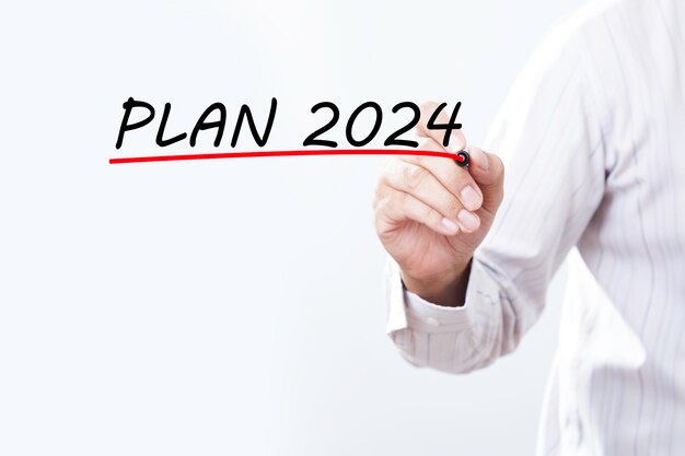 Imprenditore che scrive a mano il piano per il 2024 con un marcatore rosso su una lavagna trasparente