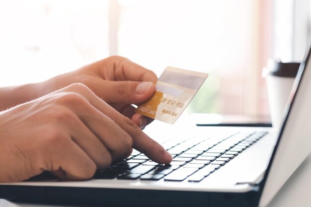 Imprenditore che tiene in mano una carta di credito con l'uso di un portatile per lo shopping online mentre fa gli ordini a casa business lifestyle technology ecommerce digital banking e concetto di pagamento online