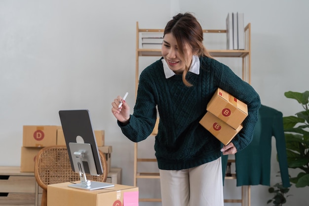 Imprenditore di piccole imprese di avvio di una donna asiatica freelance che utilizza un laptop con scatola Scatola di imballaggio di marketing online di successo allegro e concetto di idea per le PMI di consegna
