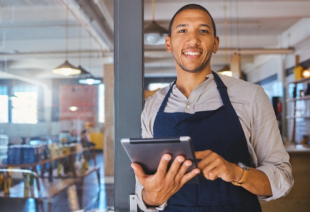 Imprenditore di ristoranti con tablet appoggiato alla porta e aperto al ritratto dei clienti Gestore del proprietario o dipendente di un negozio di fast food di avvio di una caffetteria o di una caffetteria in piedi felice con un sorriso