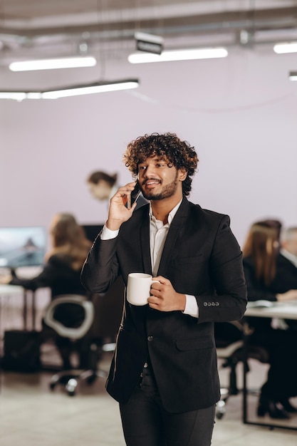 Imprenditore di successo che fa una telefonata durante la pausa caffè Impiegato occupato che tiene una tazza di caffè e usa lo smartphone